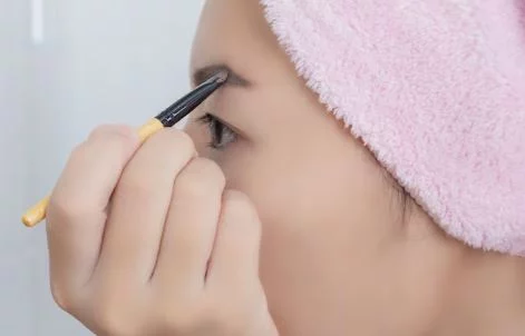 Chica aplicando con pincel polvo de cejas. Maquillaje para cejas: desde lápices hasta geles